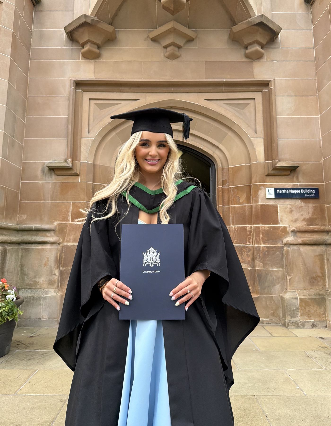 Charlotte Heron at her Ulster University graduation, in cap and gown outside the Martha Magee Building